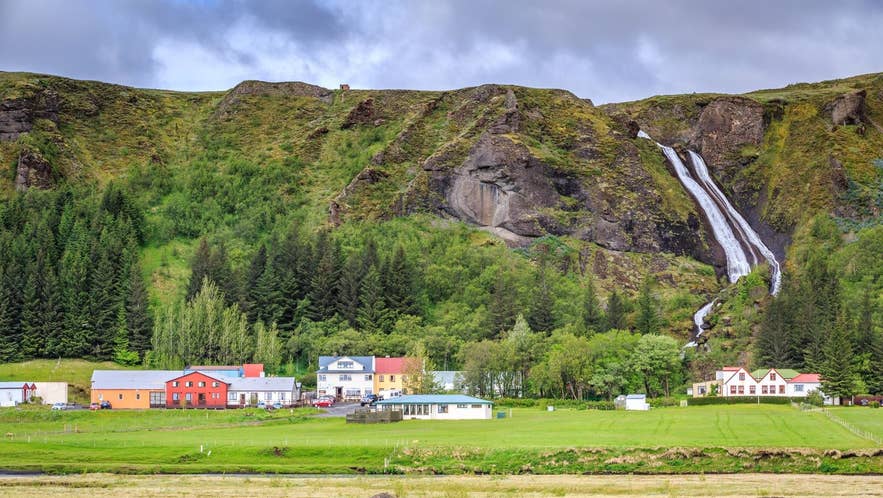 Colorful houses and a waterfall in Kirkjubaejarklaustur surrounded by green hills in Iceland in May.