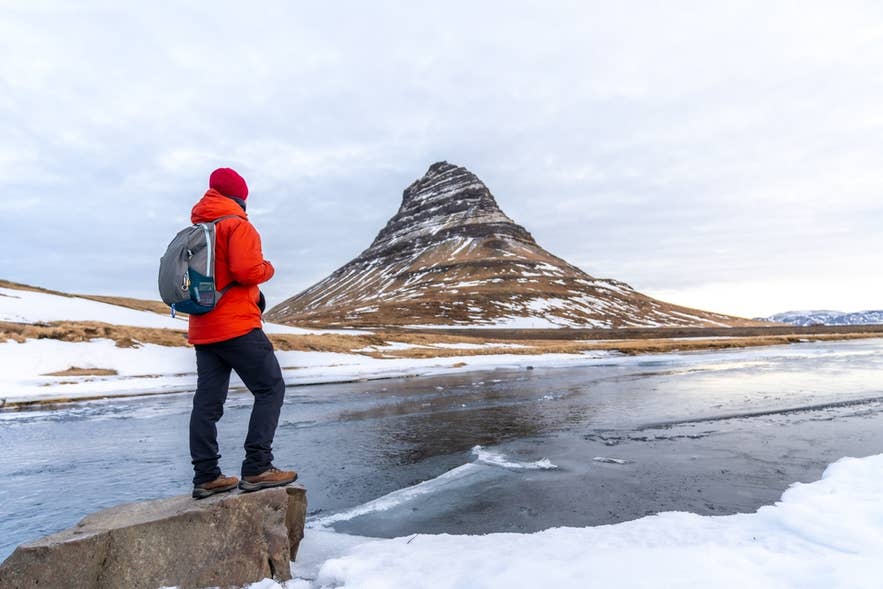 Winter hiker at Kirkjufell wearing boots, warm layers, and a red beanie shows what to wear in Iceland for snowy conditions. Winter hiker at Kirkjufell wearing boots, warm layers, and a red beanie shows what to wear in Iceland for snowy conditions.