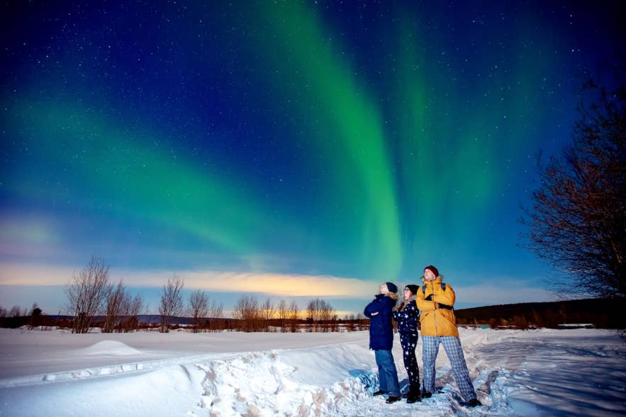 People dressed in winter layers watching the northern lights in Iceland, showing cold-weather outfits and what to wear in Iceland at night. People dressed in winter layers watching the northern lights in Iceland, showing cold-weather outfits and what to wear in Iceland at night.
