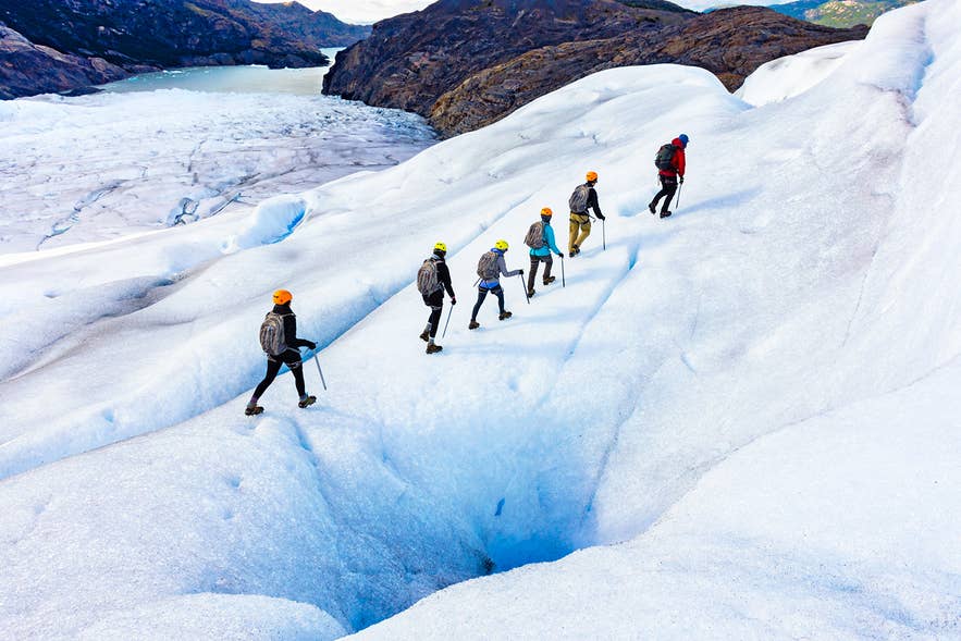 Group hiking on an Icelandic glacier wearing helmets, crampons, and layers shows what to wear in Iceland for ice adventures. Group hiking on an Icelandic glacier wearing helmets, crampons, and layers shows what to wear in Iceland for ice adventures.