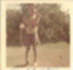 An Asian American boy wearing only shorts holds a fish in both hands, standing outdoors against a backdrop of greenery.