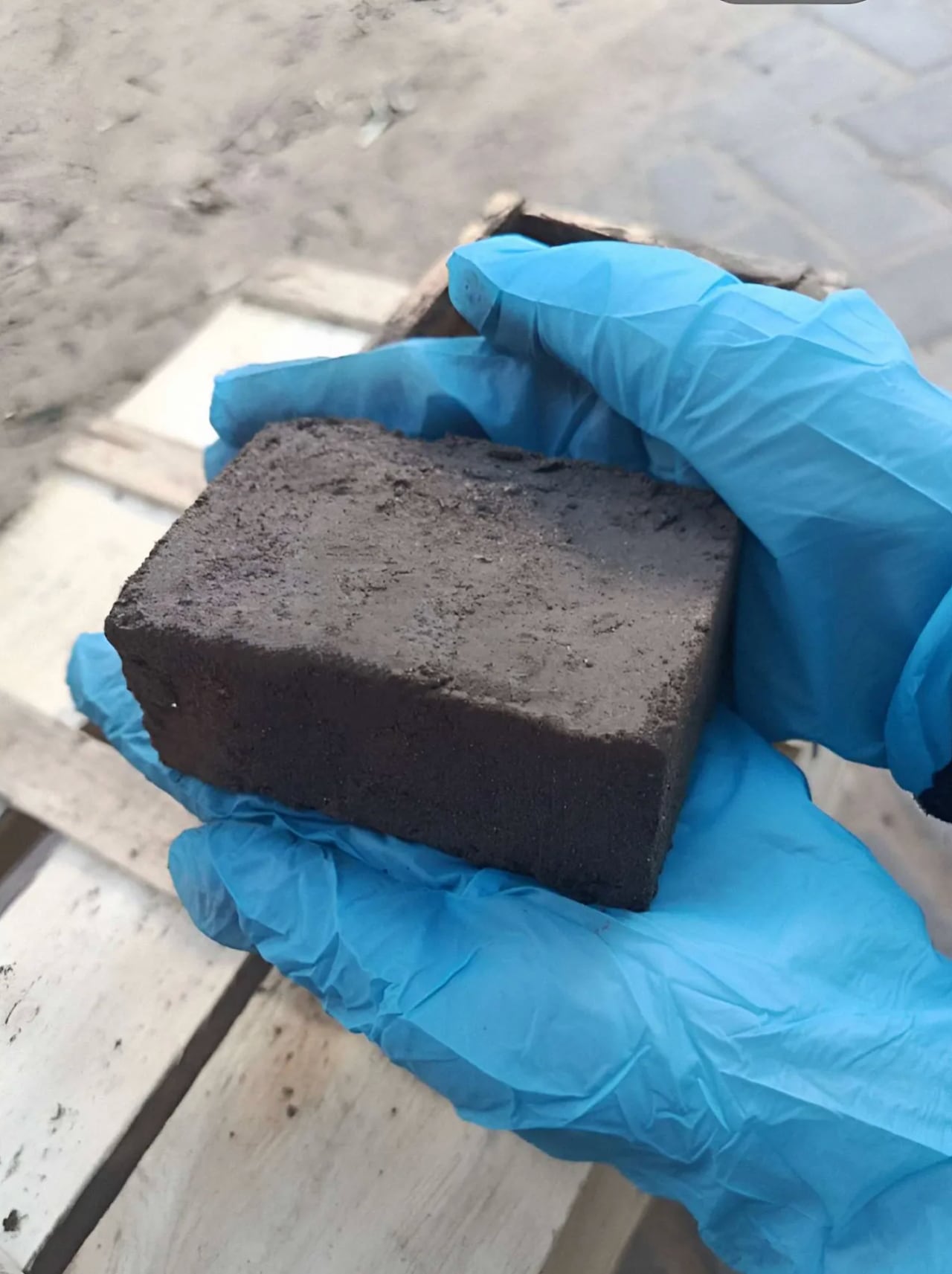 A grey brick in a blue gloved hand