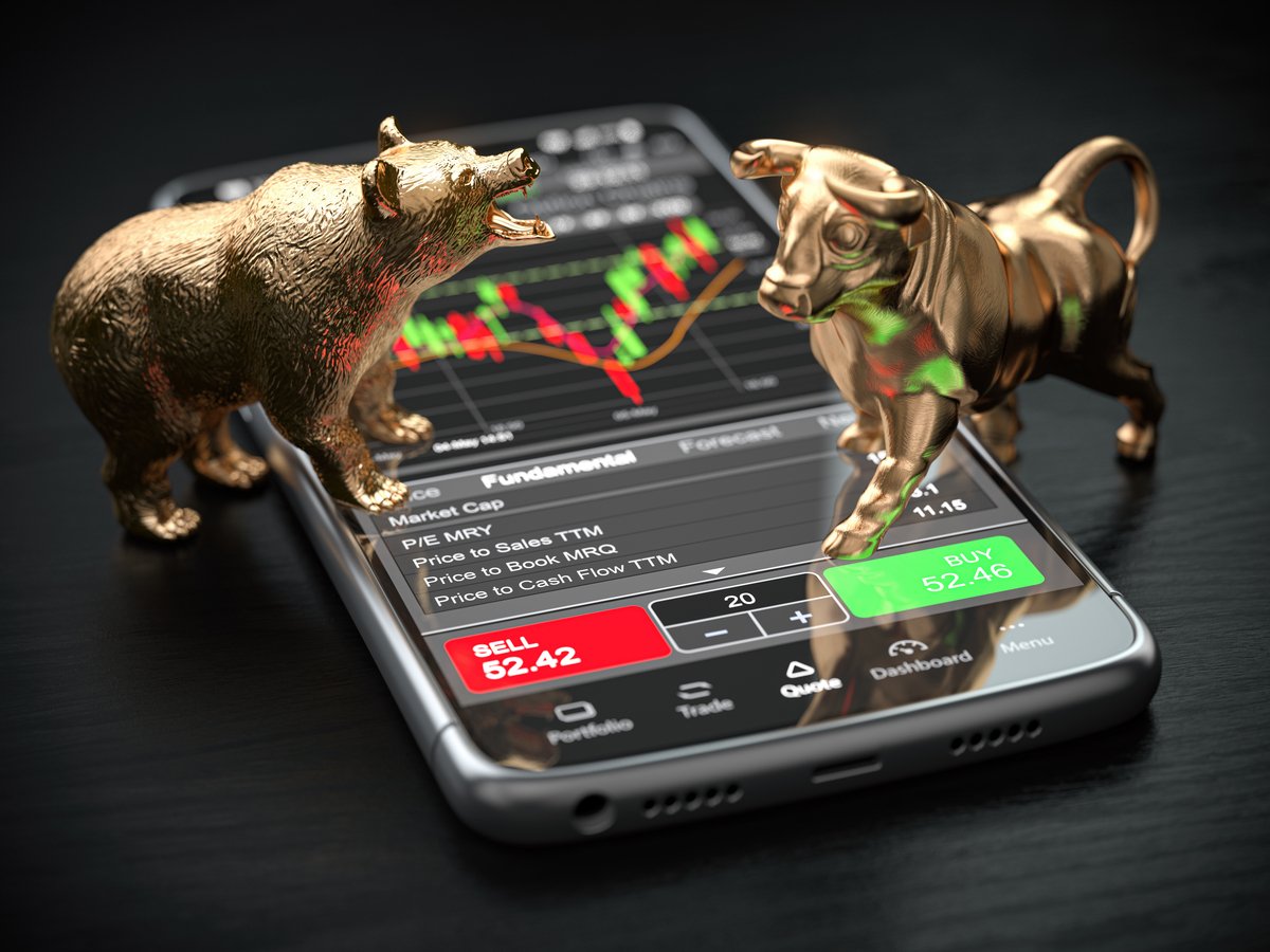 Bull and bear figurines standing on a smartphone with a brokerage app open.
