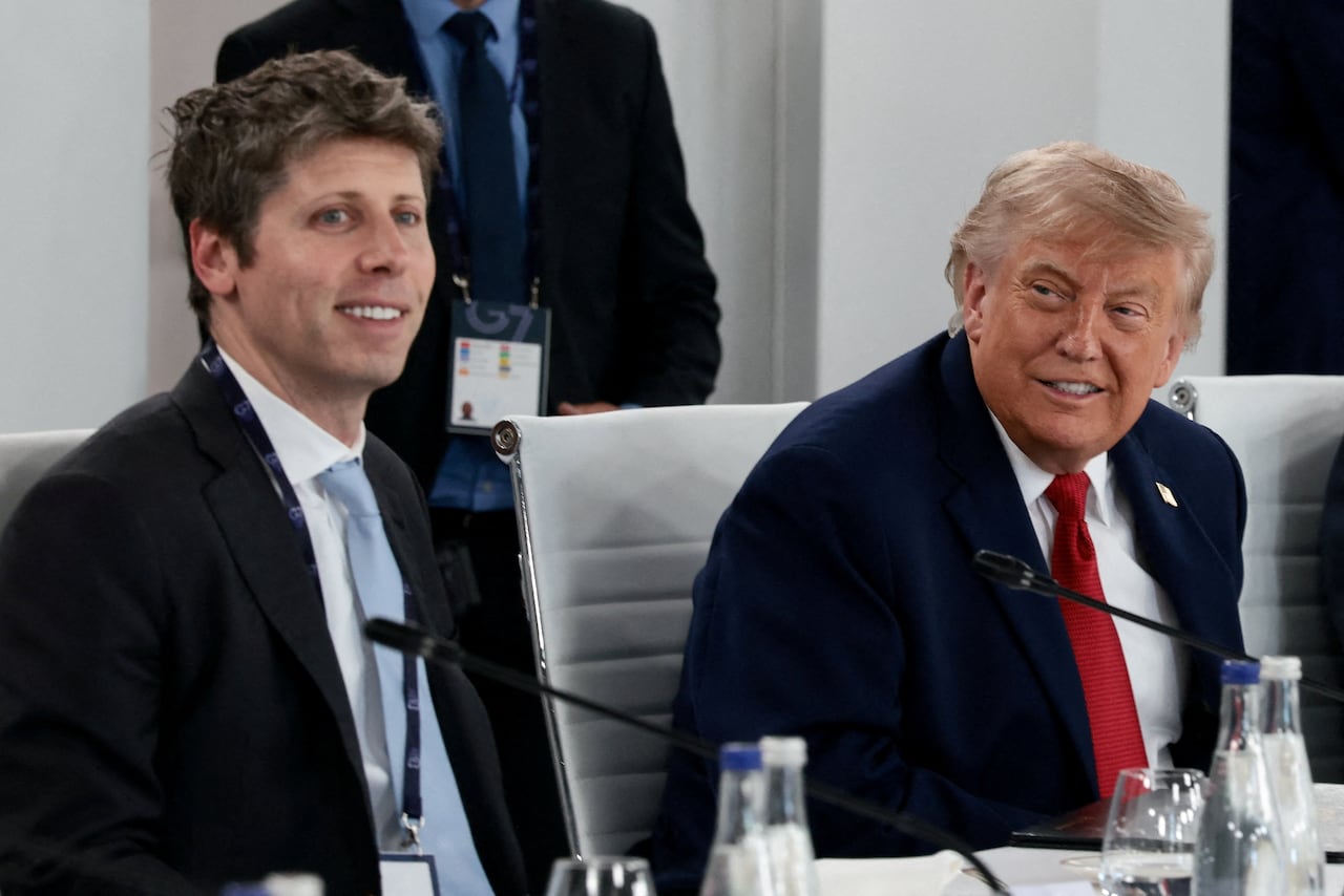 Two men wearing suits sit next to one another at a table.