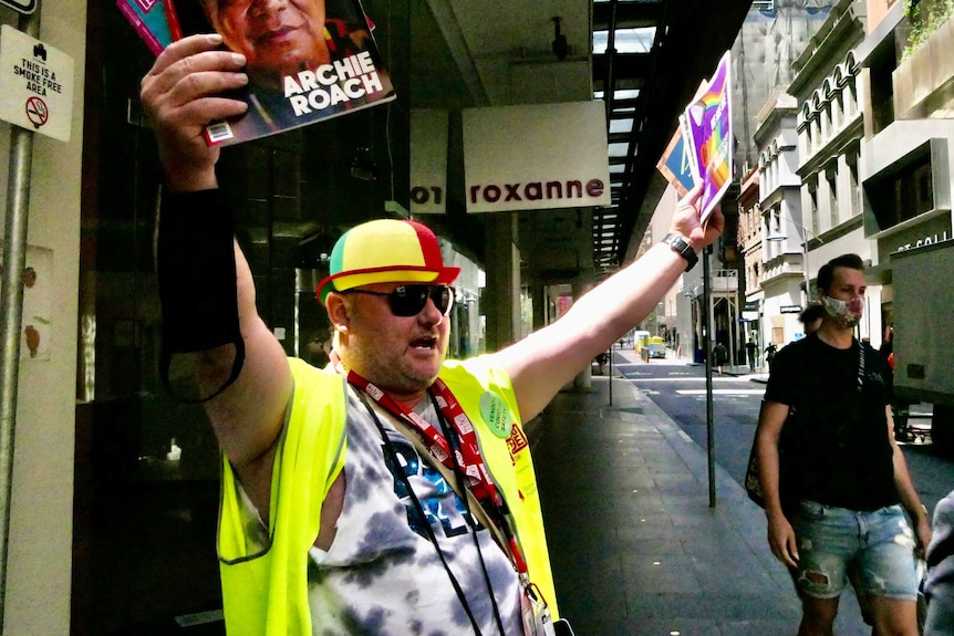 A Big Issue vendor dressed in a fluro vest and hat spruiking the magazine on the street.