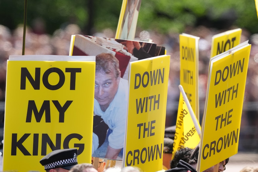 Yellow and black protest placards saying 'not my king' and 'down with the crown'.