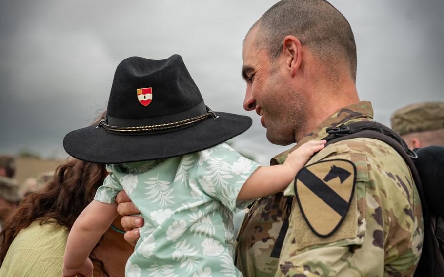 A soldier holds a baby wearing his hat.