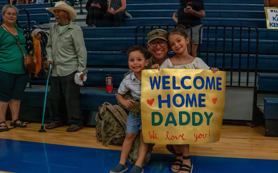 A soldier holding a “Welcome Home” sign with two kids.