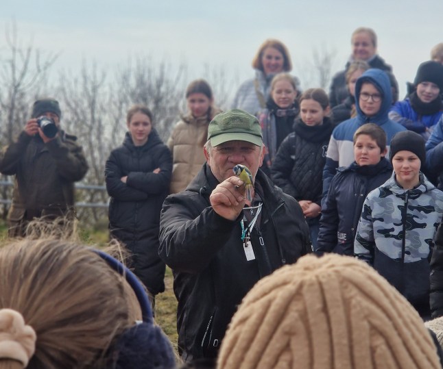 A birdringer holds a tiny migratory bird in the middle of a crowd of people in Palanga, Lithuania