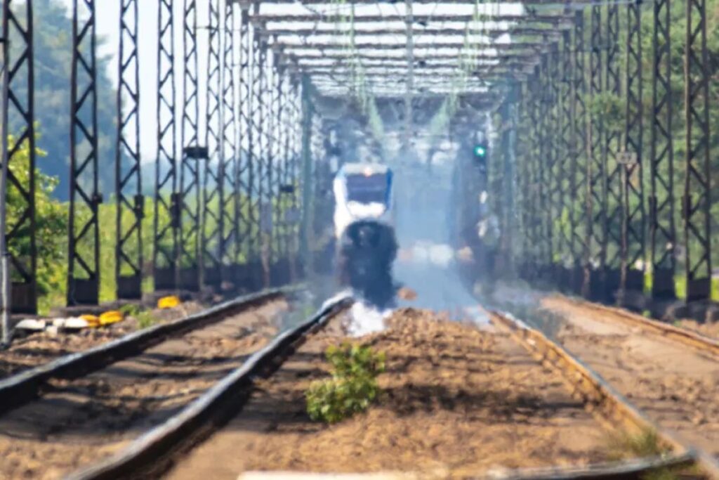 Passenger rail companies in Europe and heat wave passenger train on railway track crossing a metal truss bridge in summer heat haze