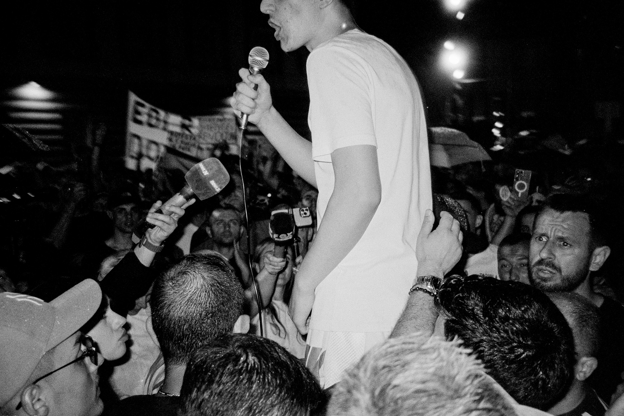 Crowd of protesters with man holding a microphone being lifted above the crowd.