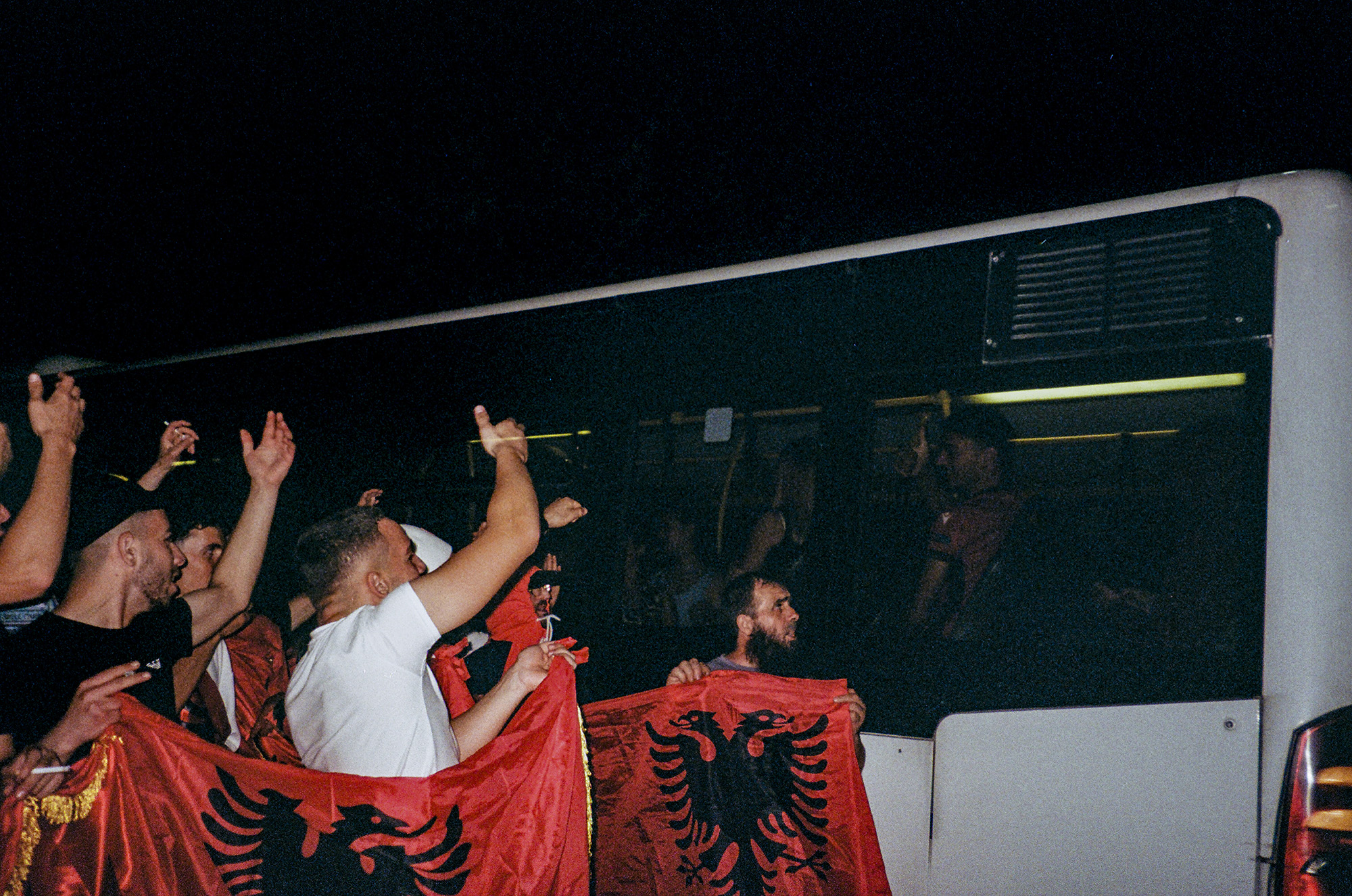 Crowd of protesters holding flags waving at a passing bus.