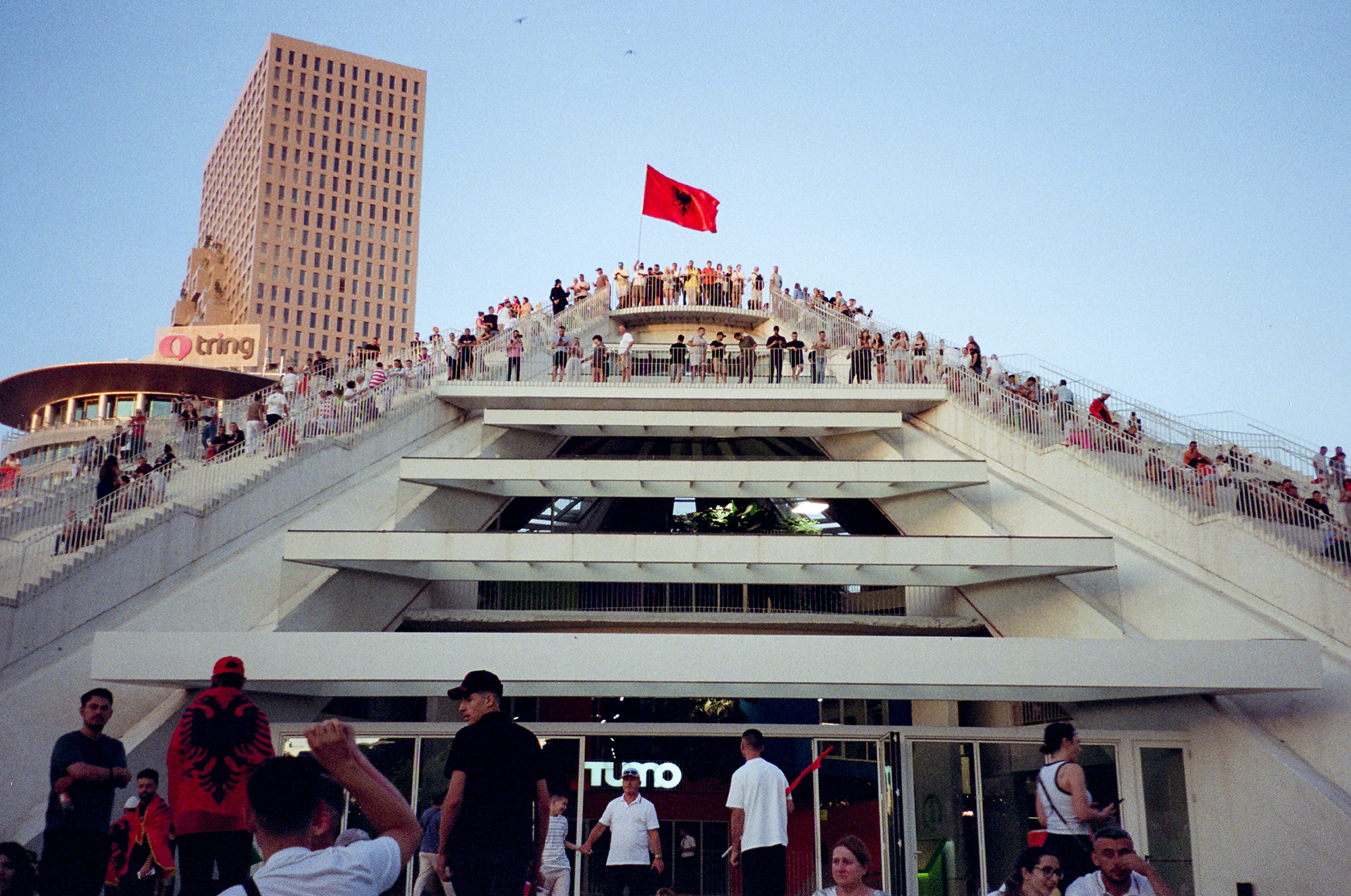 Crowd of protesters stand on the stairs of a pyramid shape building.