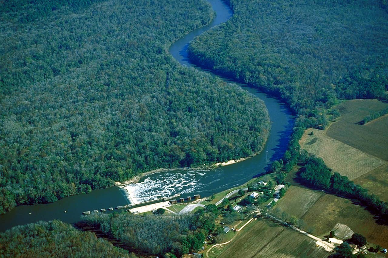 shows low level satellite photo of a dam feeding into a river, surrounded by trees