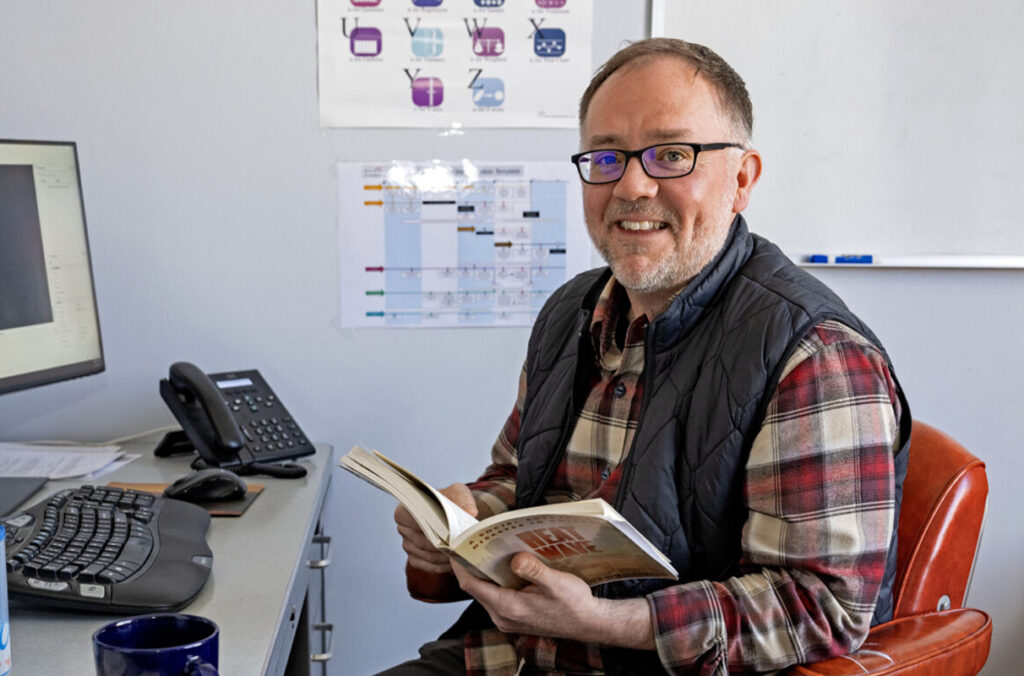 WSU professor Justin Denney sitting at a desk with an open book.