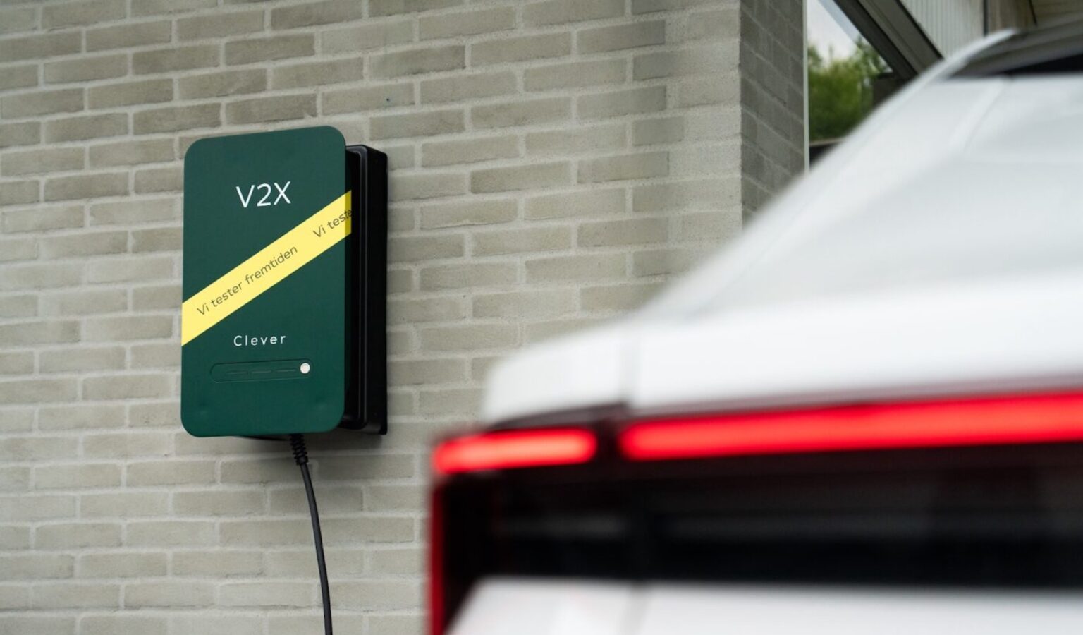 Denmark wants EVs to power homes, rescue blackouts, and feed the grid in new pilot A green wall-mounted electric vehicle charger next to a white car.