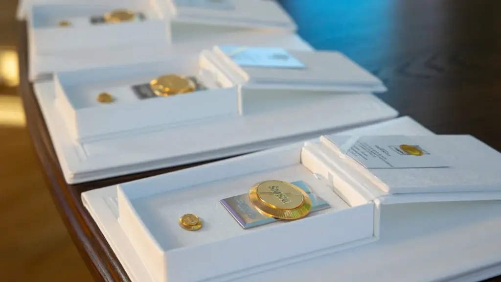 Lithuania Education Ministry Honour Nominations Ant stalo išdėliotos atviros baltos dėžutės su auksiniais ženkliukais bei sertifikatais viduje.
