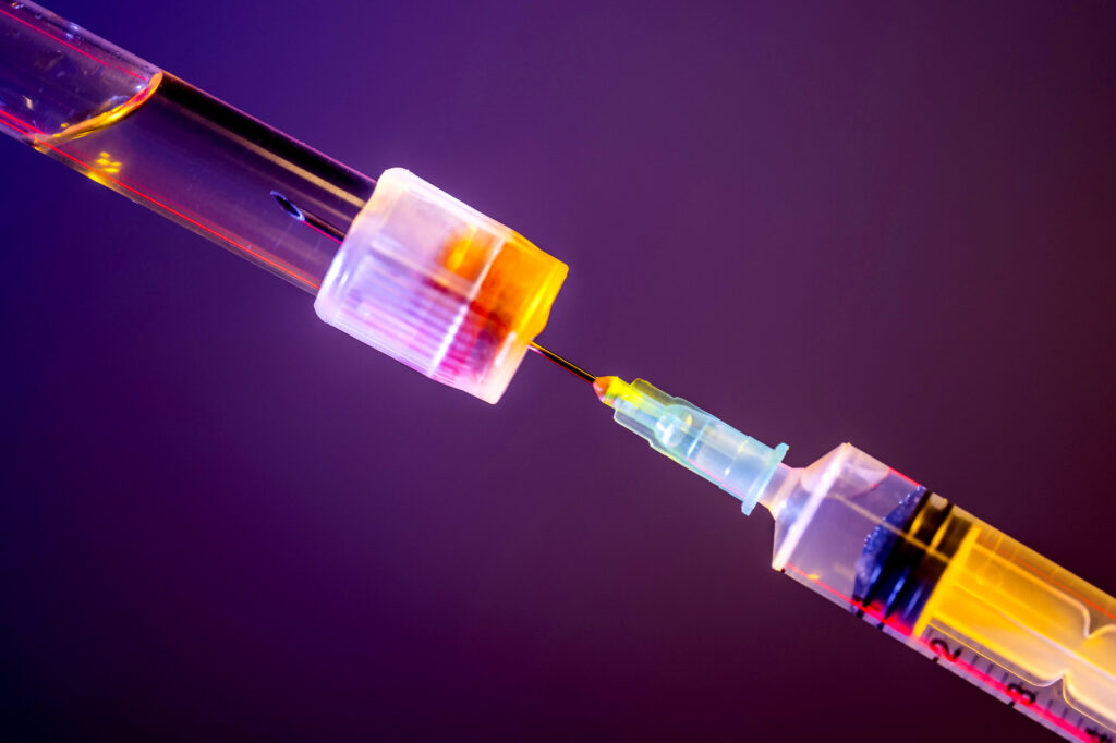 Peptides for Anti-Aging: Benefits, Risks and What Experts Say A syringe draws a substance from a tube. It is lit against a purple backdrop.