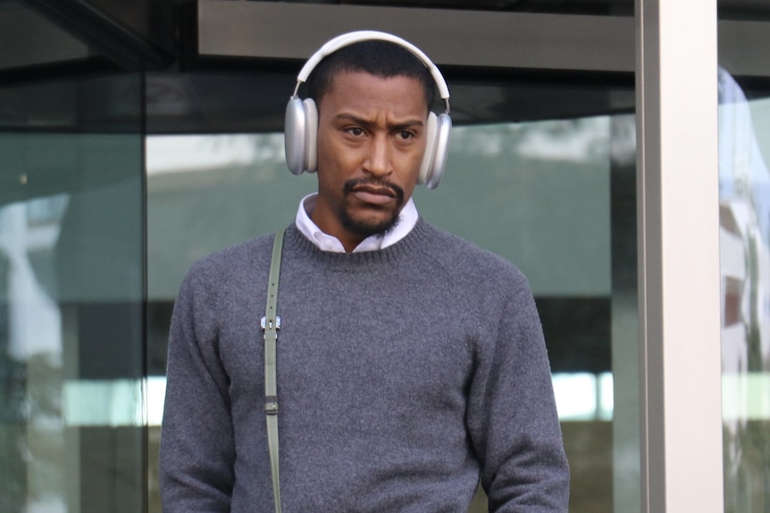 A man with white headphones stands at the top of courthouse stairs.