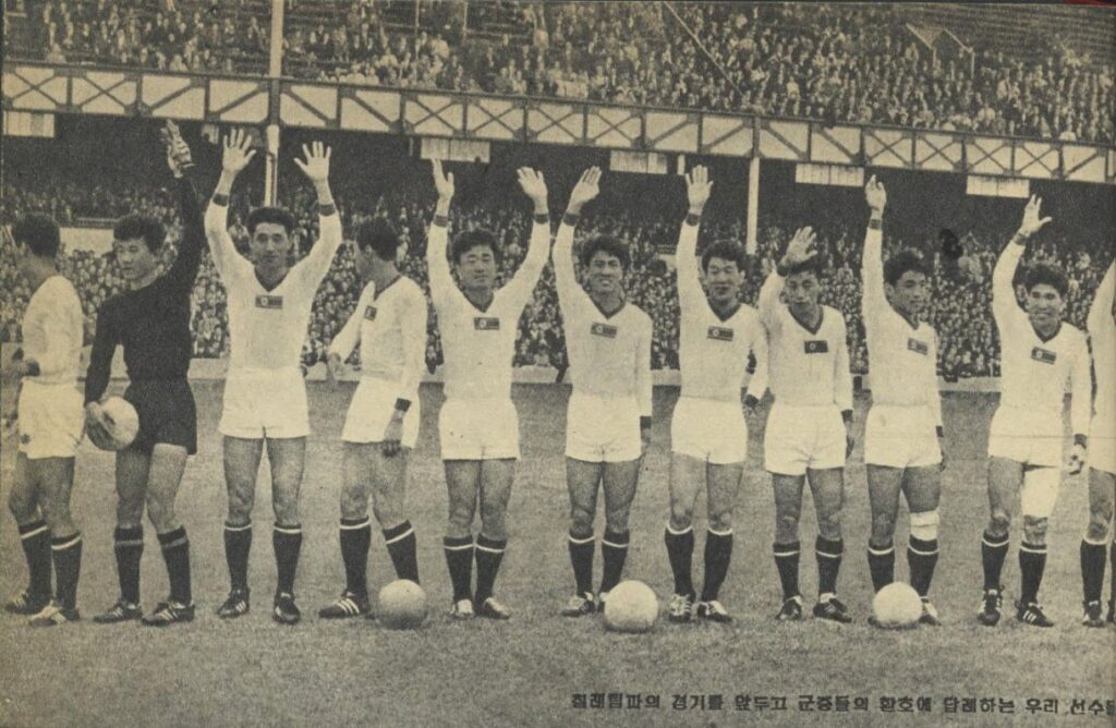 Eleven soccer players are lined up in a row, waving to the audience.
