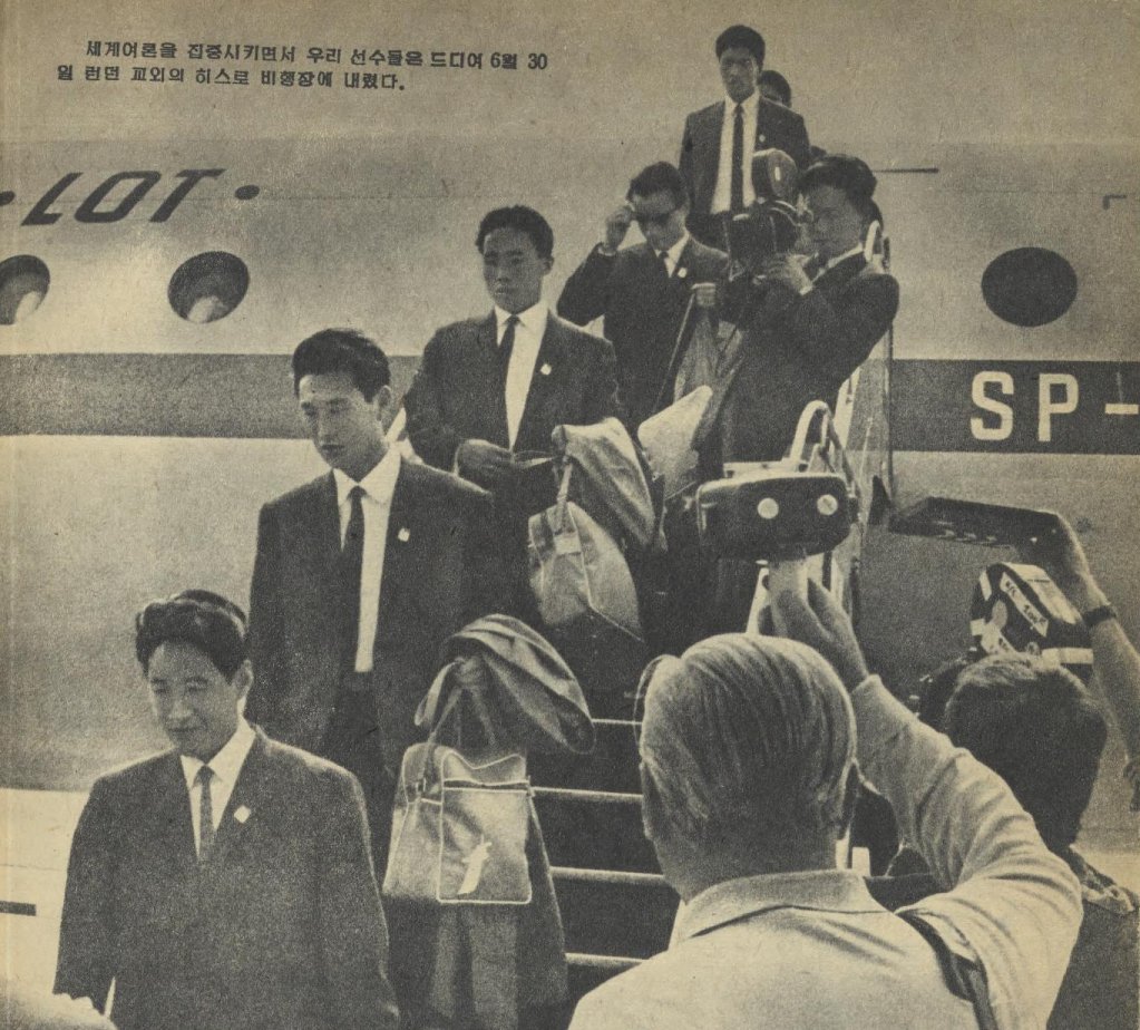 Several men descend stairs, exiting an airplane. To the right are men on the ground holding cameras.