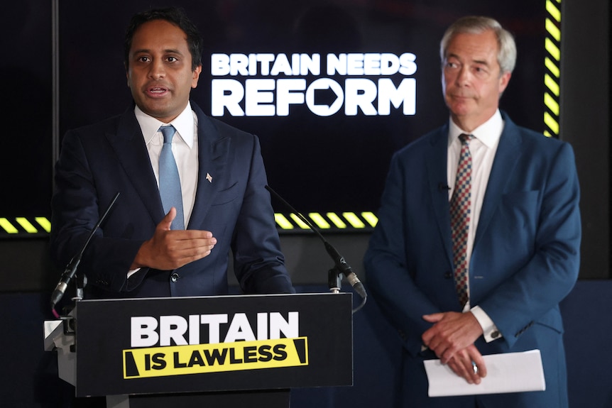 Zia Yusuf (left) and Nigel Farage stand in front of a sign which reads Britain Needs Reform.