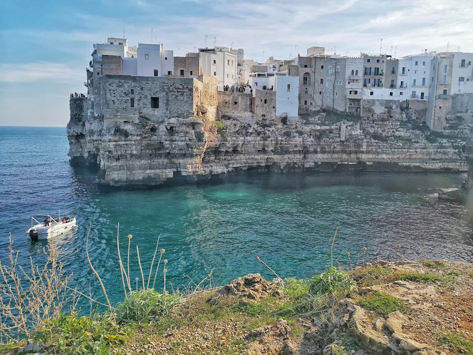 View of Polignano a Mare's whitewashed buildings perched above cliffs along the Adriatic Sea in southern Italy's Puglia region.