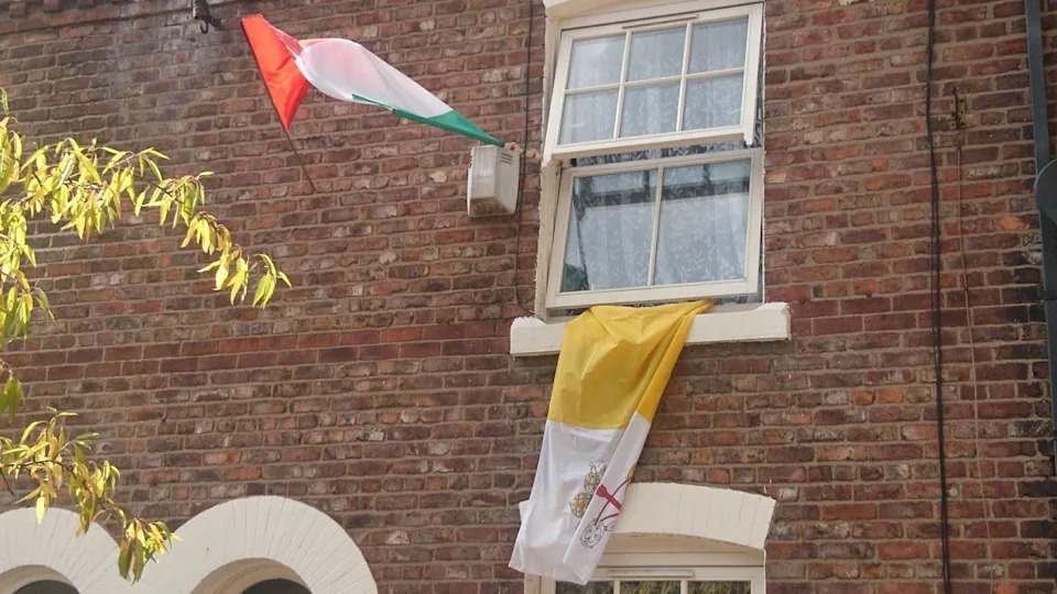 A red, white and green Italian flag and a yellow and white Vatican flag with the HOly See's coat of arms fly from a house in Little Italy, Ancoats, Manchester.