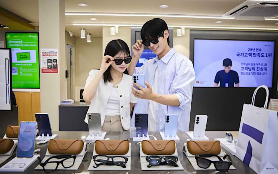 a woman and a man wearing Meta’s Ray-Ban AI Glasses and taking a selfie or checking how they look with a phone.