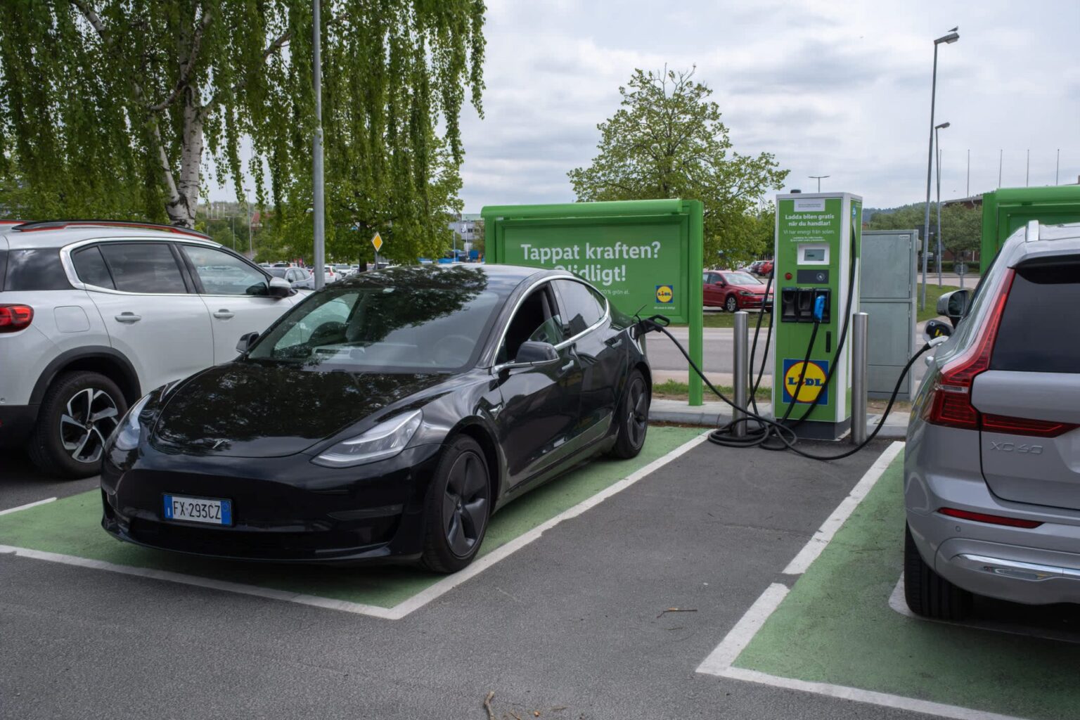 Cheaper Tesla Model 3 pack beats pricier nickel batteries in Sweden used-EV analysis A black Tesla Model 3 charging at an electric vehicle station next to a silver SUV in a parking lot.