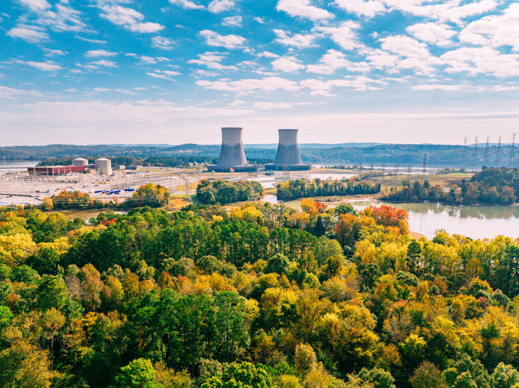 Prediction: These Will Be the 2 Best Nuclear Energy Stocks to Buy for the Next 5 Years Two cooling towers are shown far off in the horizon surrounded by a dense forest of trees.