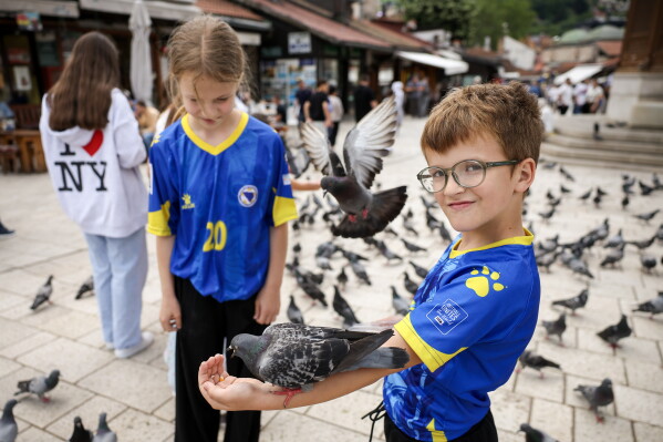 Children in Bosnian national soccer team jerseys feed pigeons in the old part of Sarajevo ahead of the soccer match of the FIFA World Cup 2026 between Canada and Bosnia, in Sarajevo, Bosnia, Friday, June 12, 2026. (AP Photo/Armin Durgut)