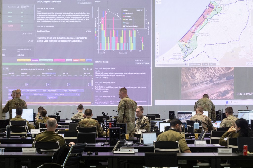 Military personnel and international officials monitoring screens displaying maps and information about the Gaza Strip at the Civil-Military Coordination Center.