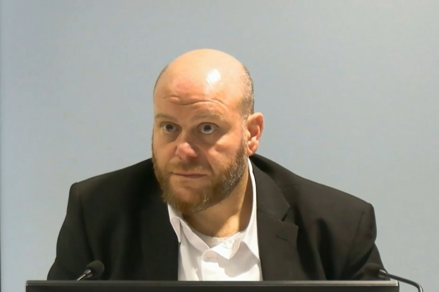 Sheikh Alsuleiman sitting at a desk speaking into a microphone looking serious.