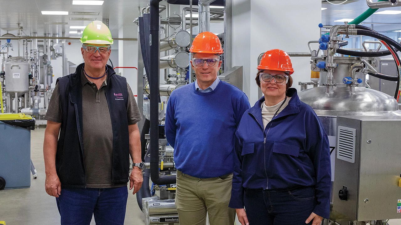 Three people in hard hats and safety goggles stand with chemical separation equipment.