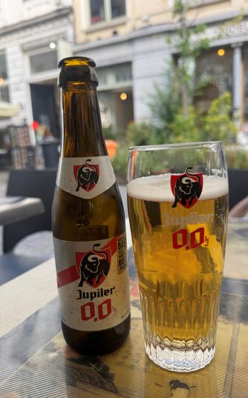 Pint of Jupiler 0.0 next to an empty beer bottle on a table