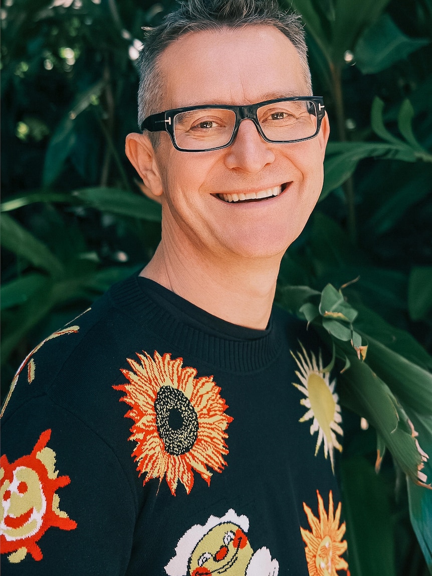 A man wearing glasses smiles and looks at the camera