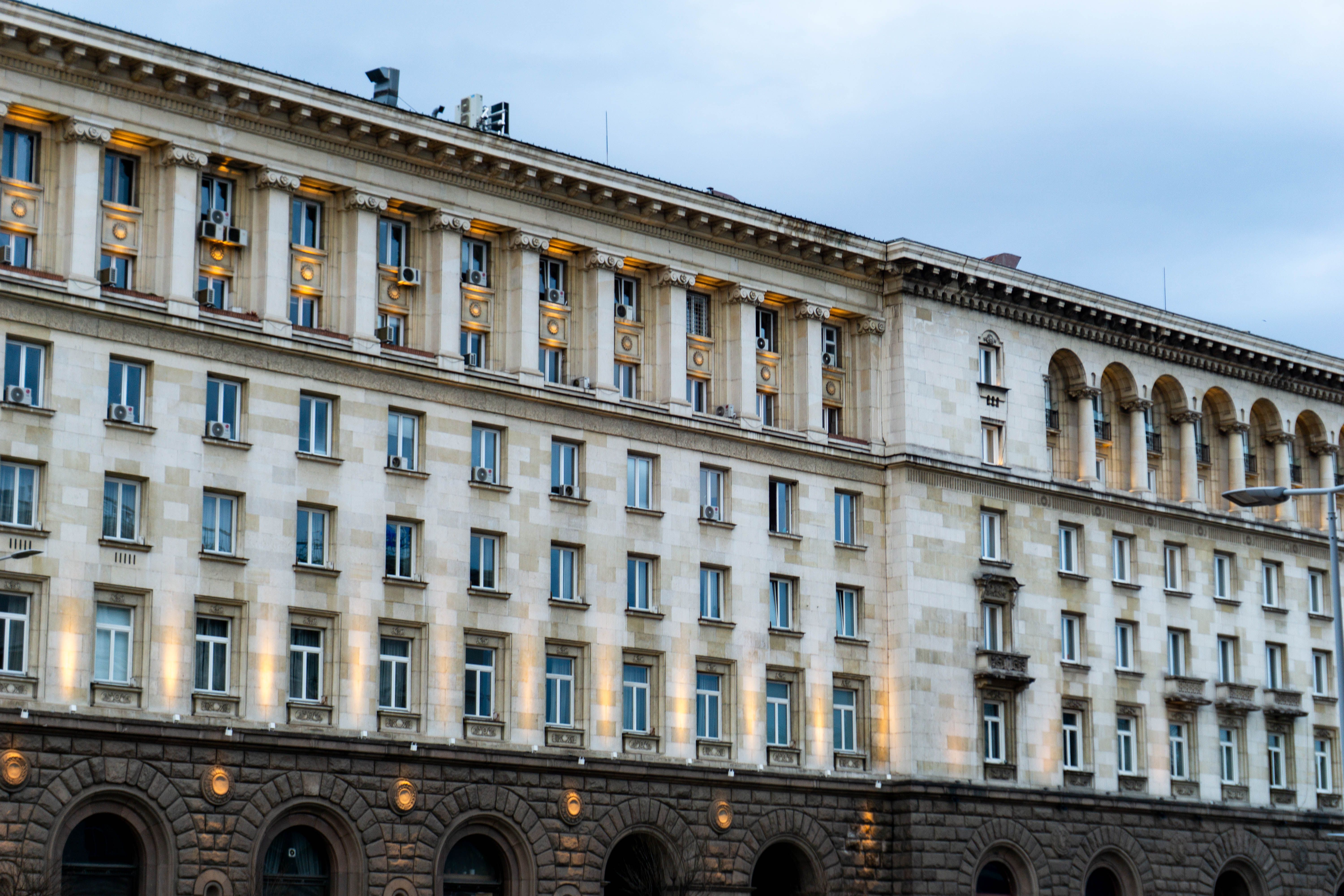 Illuminated stone government building with rows of windows and arched openings under a cloudy sky