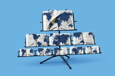 A black music stand holds multiple open songbooks against a solid light blue background. On the pages of the open books, blue world map patterns overlay the printed musical notes. The stand features a tiered layout, with a large music book on the top ledge and smaller books arranged across the lower ledges.