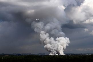 A passenger plane flies past smoke rising from a Wildberries warehouse outside St. Petersburg. July 24, 2026