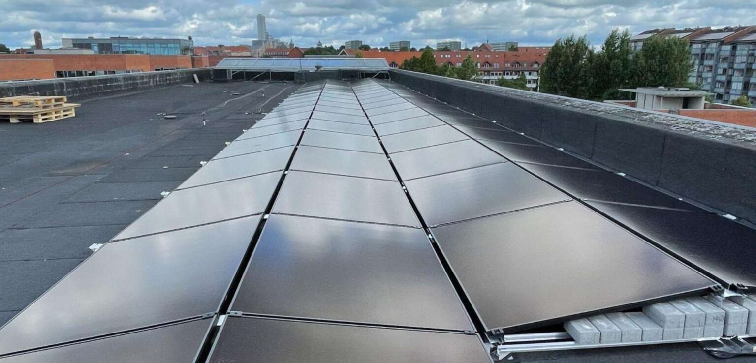Denmark solar cooperative lets members co-own university rooftop solar, collect yearly returns Solar panels installed on a building rooftop with gray clouds in the background.