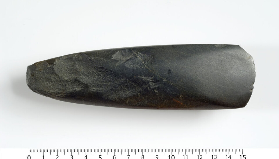 Dark elongated stone artefact positioned above a metric ruler on a plain background.