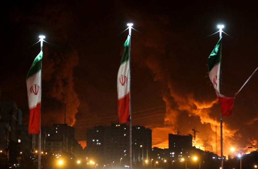  Iranian flags fly as fire and smoke from an Israeli attack on Sharan Oil depot rise, following Israeli strikes on Iran, in Tehran, Iran, June 15, 2025. 