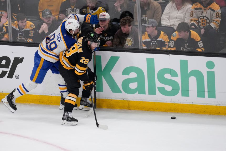 The Boston Bruins' Elias Lindholm and the Buffalo Sabres' Alex Tuch battle for a puck near a Kalshi ad in Boston in April.