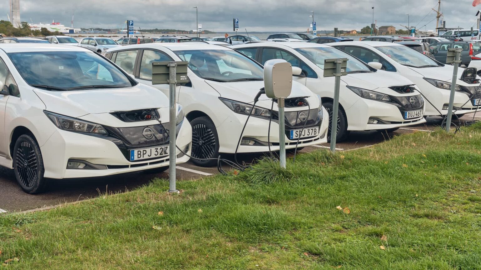 EU analysis finds used EVs are retaining value, and that could be inflating lease payments A row of white electric cars parked at charging stations in a parking lot.